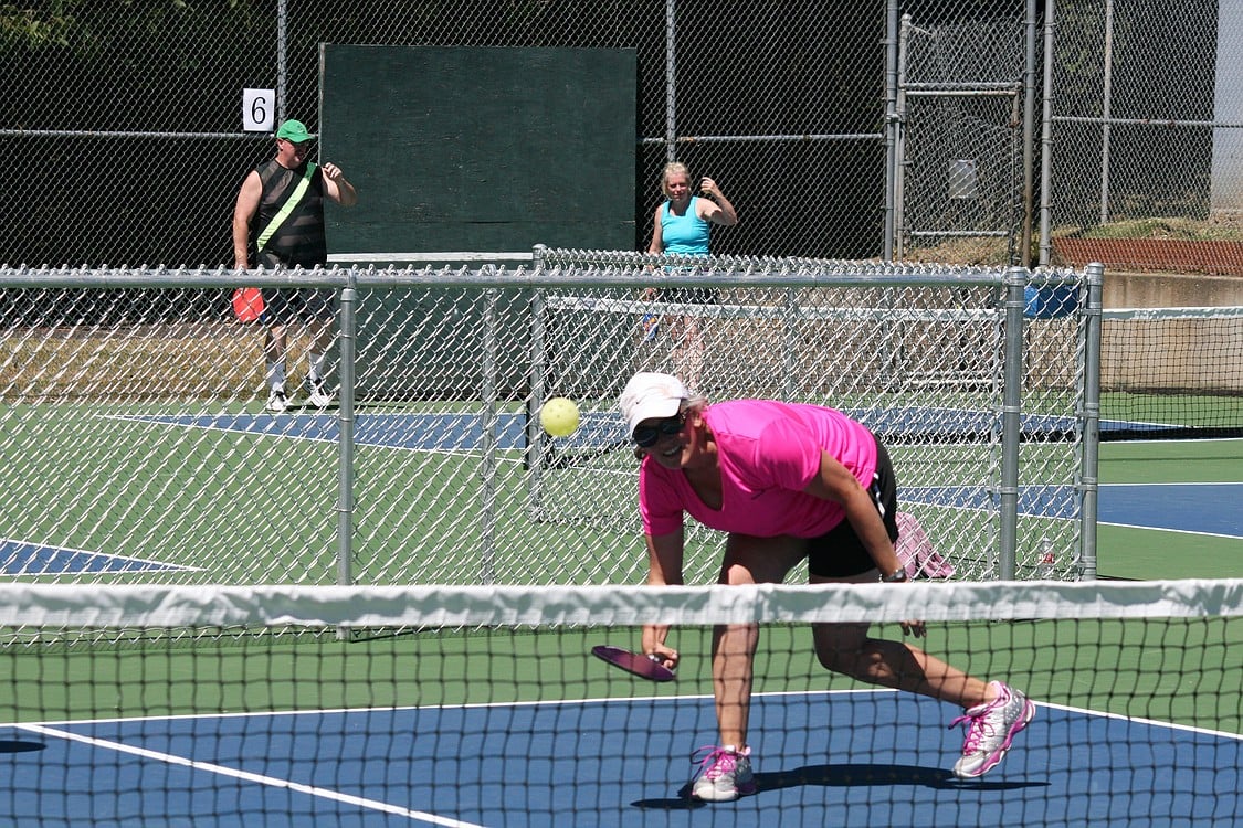 Michelle Annett digs up a pickleball, while RD Fisher and Kathy Rambousek celebrate after scoring a point in the background. The Washougal Pickleball Mixer brought 96 players, and their friends and family members, to the city's six new courts at Hathaway Park.