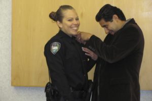 George Hernandez pins a Camas Police Department badge on his wife Monica Hernandez Thursday morning as she is officially sworn in as its most recent patrol officer hire.