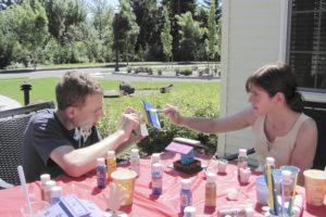 Anthony Overacker and Kendra Upjohn decorate birdhouses during a recent craft day on the patio at Columbia Ridge assisted living. The facility sponsors these types of gatherings every month so residents and community members have a chance to mingle. Below, at left, Heidi Alandt, activities director, gets to work and at right, Ashima Ram, community outreach coordinator, puts a splash of color on her creation.