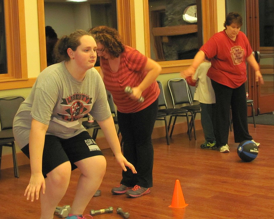 Paula Yeager does squats on the Bosu ball, while other participants work with weights and a weighted ball in the background.