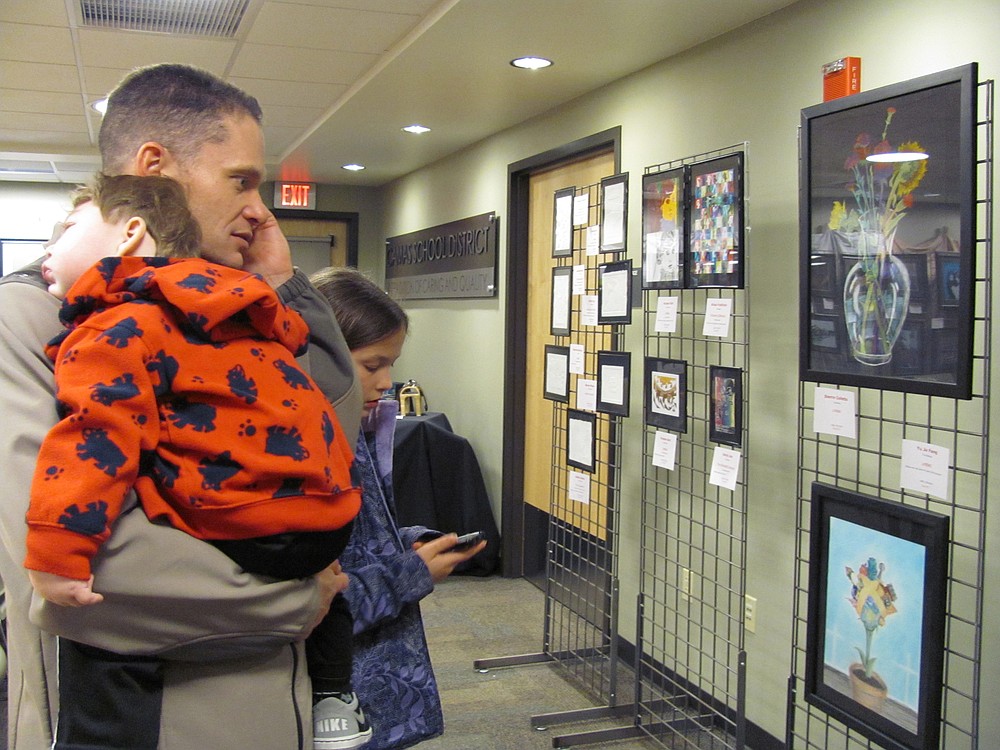 Jeff Snell, Camas School District assistant superintendent, listens to students describe their work at the CHS art show via a recording by dialing a specific number associated with each piece. His daughter, Mackenzie, does the same while son Micah takes a nap.