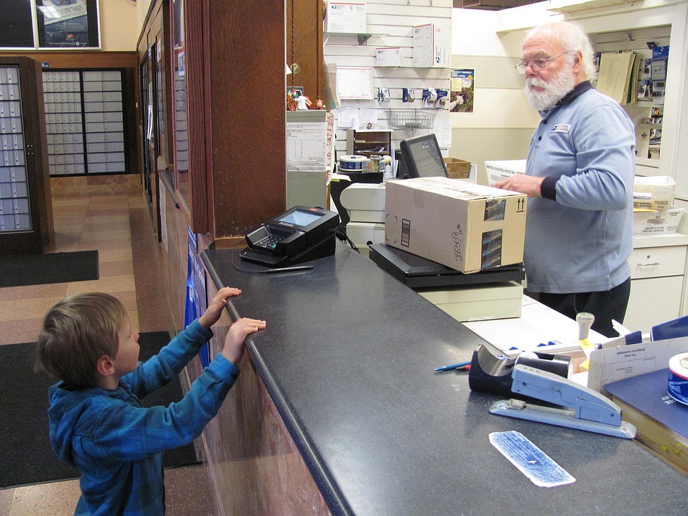 Dan Smith talks with the son of one of his postal customers, at the post office, in downtown Camas. Smith has collected several wind-up toys to show to children. He has worked for the United States Postal Service for 33 years, in the local office.