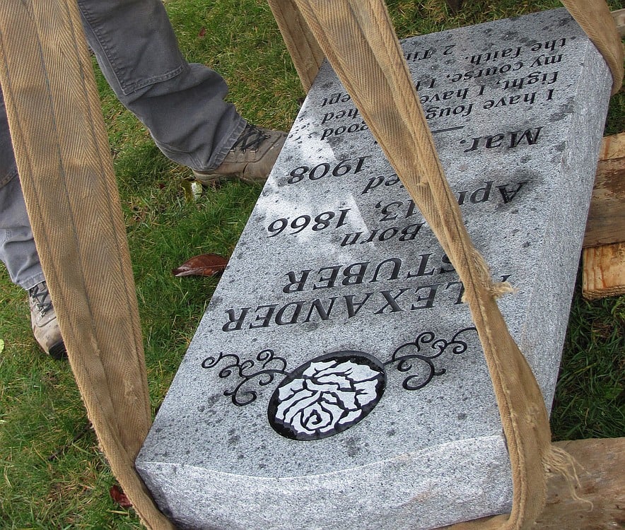 The new headstone of Alexander Stuber is carefully lowered into place, using a flatbed truck crane and pulley, at the Camas Cemetery on Friday.