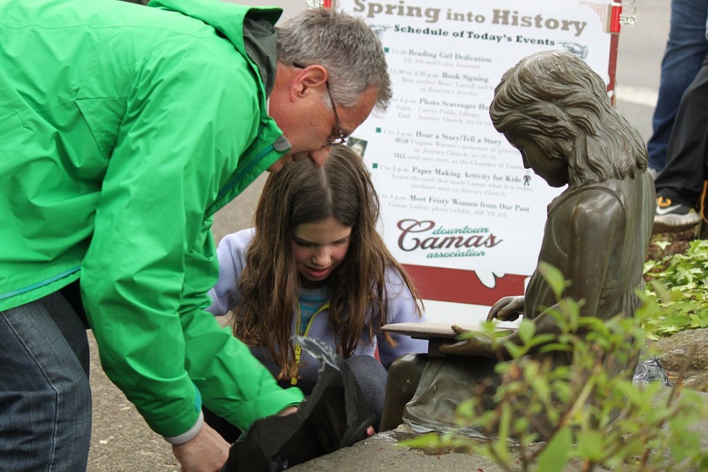 Grandfather and granddaughter, Randy Curtis and Olivia Brotherton, help remove the plastic from the newly refurbished reading girl statue. They spearheaded efforts to replace the statue's book, which was stolen more than a decade ago. City officials, local leaders and citizens attended the unveiling ceremony on Saturday.