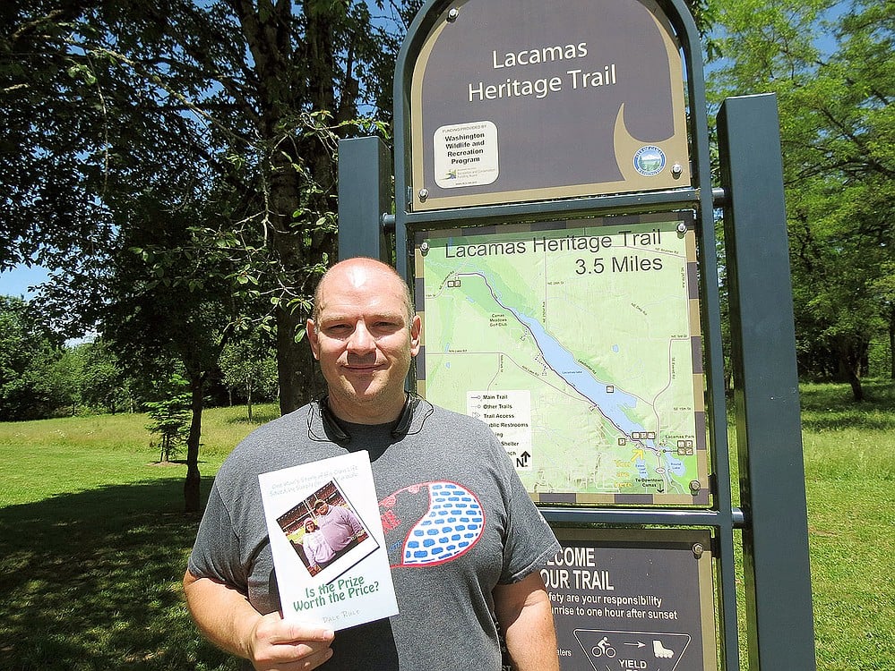Dale Rule holds up a copy of his book, "Is the Prize Worth the Price?," after walking the Lacamas Heritage Trail. The 43-year-old said he has been on this stretch so many times, he could probably walk it blindfolded "without falling into the lake, hitting a tree or getting lost."
