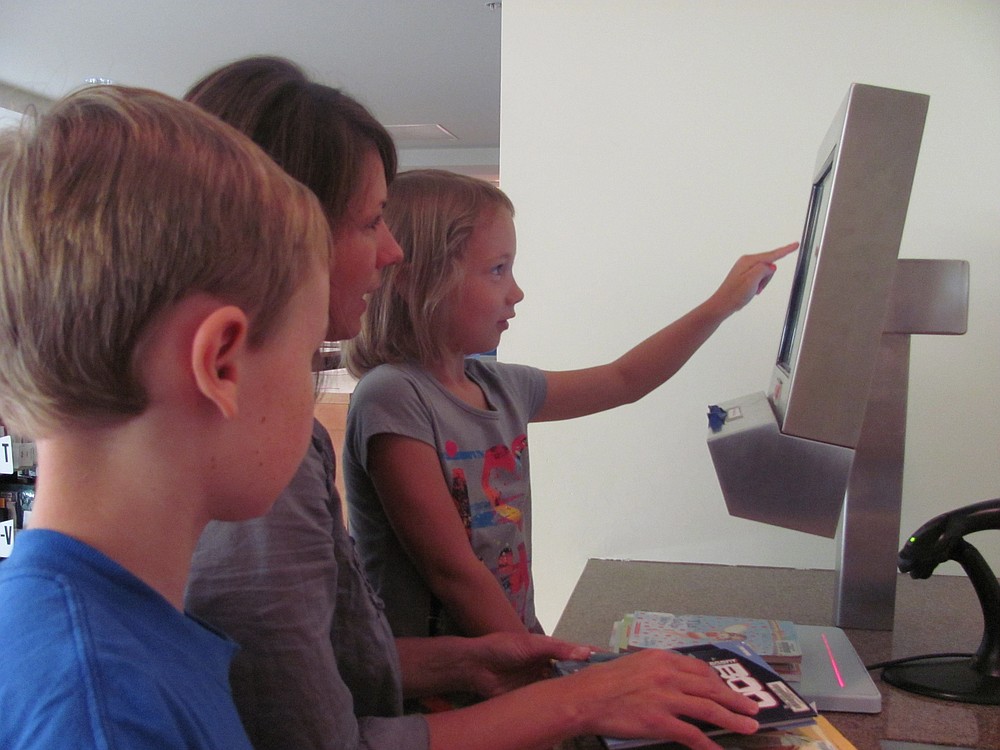 Faith Reed checks out a book from the Camas Public Library while her mom, Cammie, and older brother, Spencer, look on.