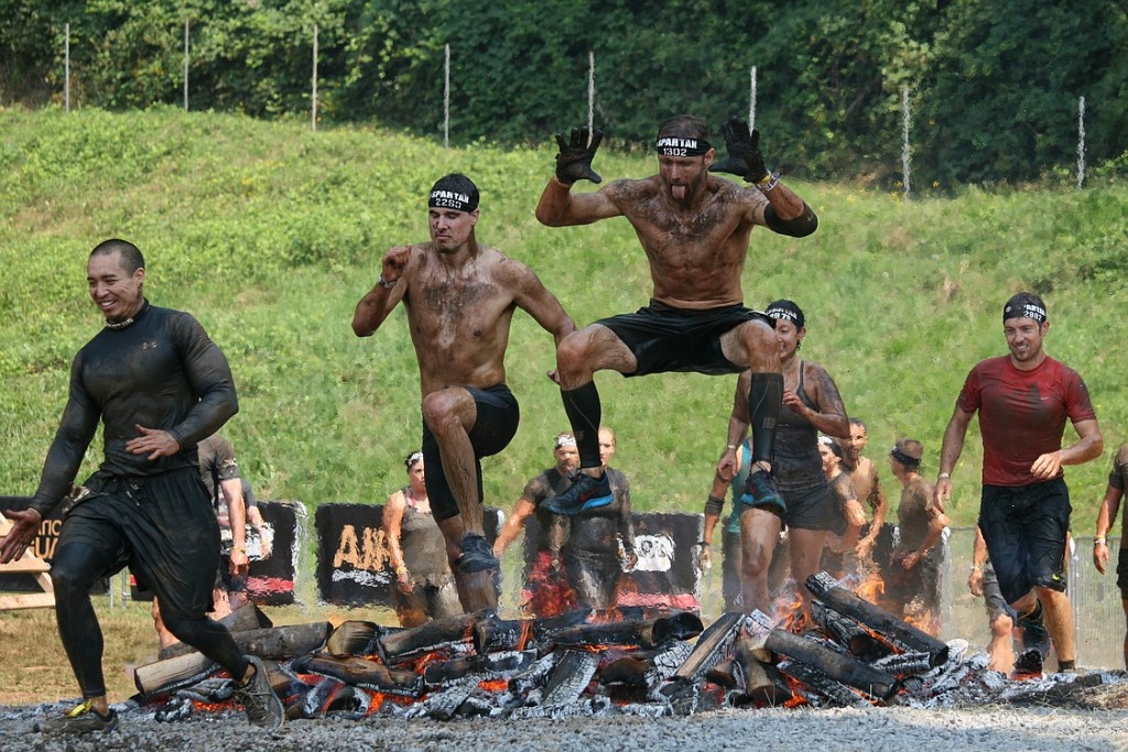 Spartans hurdle over a fire pit and head to the finish line with smiles on their faces after a day of pushing themselves to the limit.