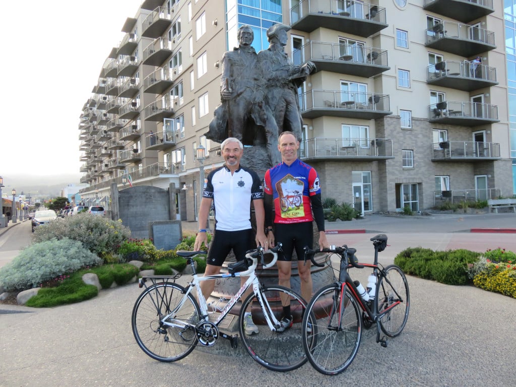 Tom Baltes and Eric Uhlberg start their cycling journey by posting near a sculture of Lewis and Clark in Seaside, Ore. 