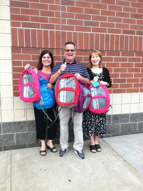 From left, principals Laura Bolt, Rex Larson and Mary Lou Woody display backpacks their schools received, filled with supplies, for children in need.