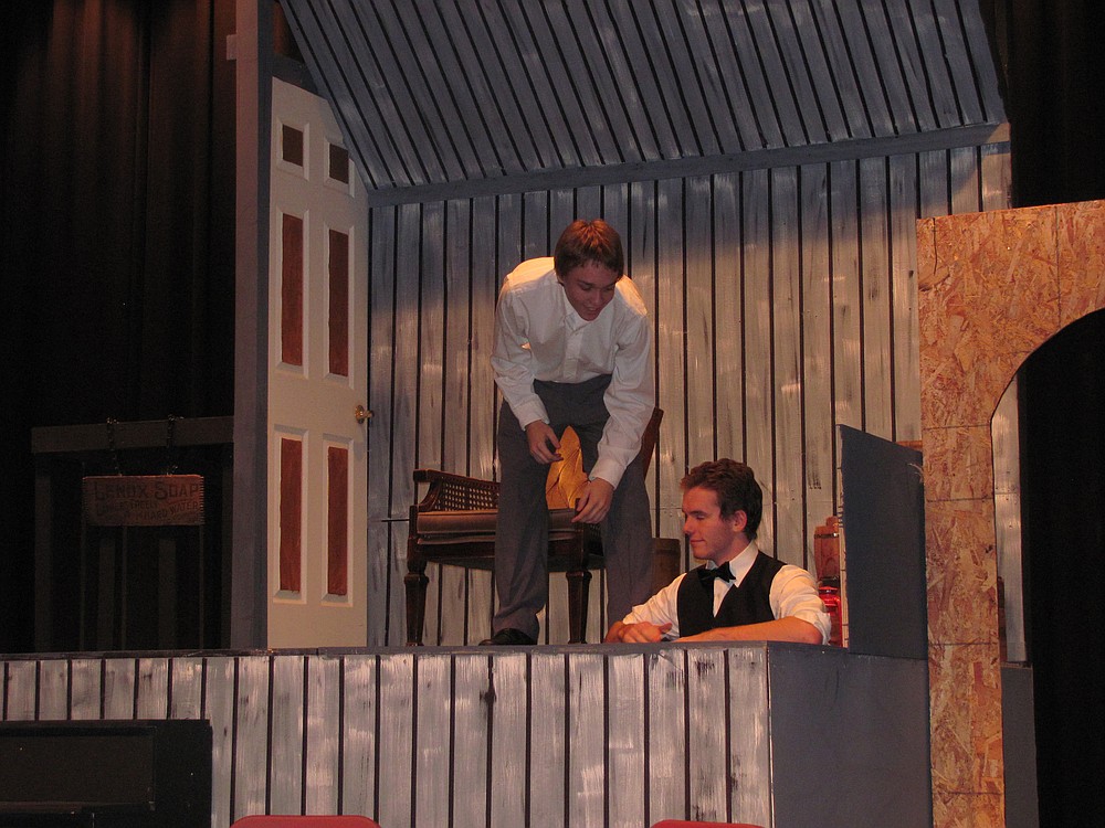 Branaby (Tyler Schroeder, standing) and Cornelius (Mac Wright in the trap door) try to explode some tomato cans to get out of a day of work.