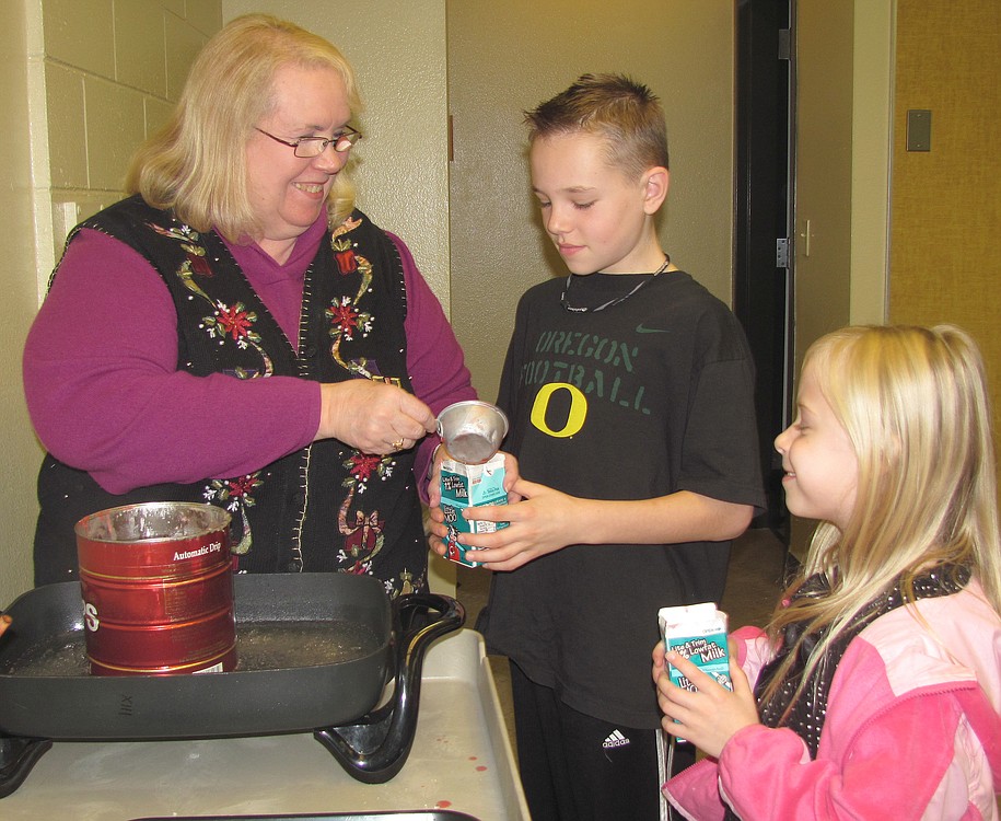 Community Education winter camp coordinator Barb Heckman helps Caden Wengler and Lexi Lienzle make candles.