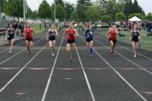 Karsyn Quade (center) bursts to first place in the 100-meter dash April 26, at Cardon Field. The Camas High School junior also won the 200 and anchored the 400 relay team to victory against Skyview and Mountain View. 