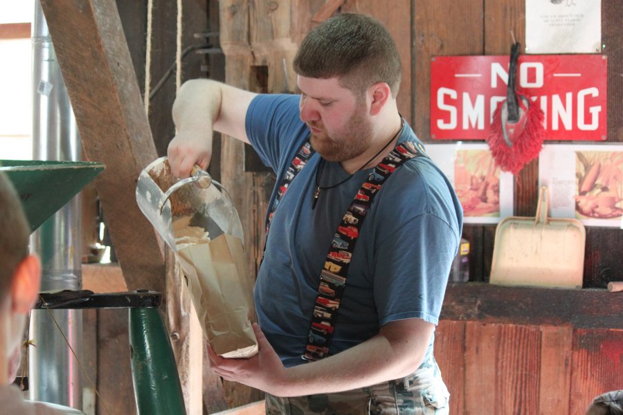 Volunteer Ian Frew scoops up the flour from the Buhr mill, and dumps it into bags for visitors to take home.