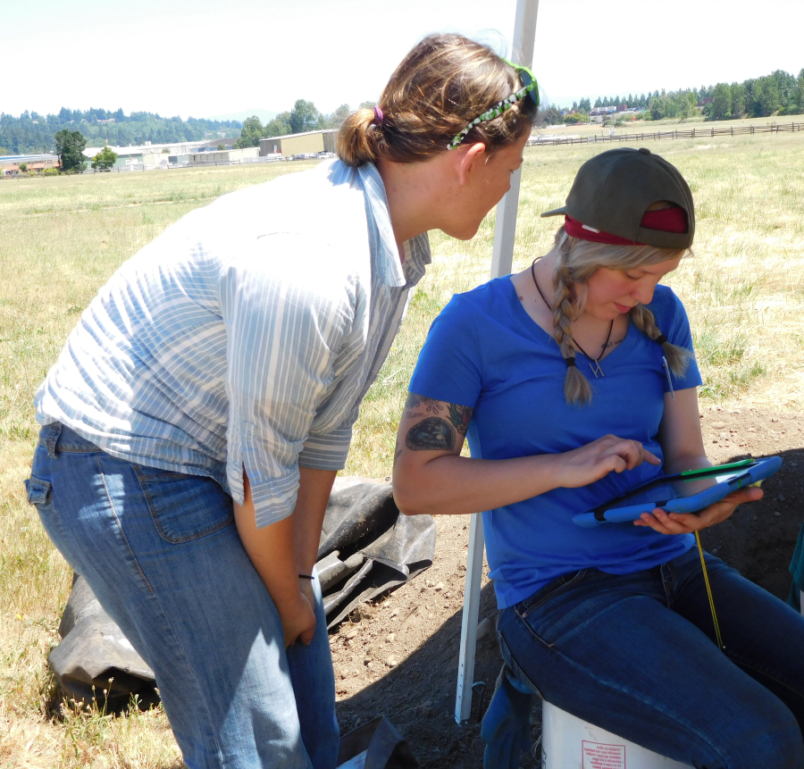 Students Efflie Helmers and Idah Whisenant compare notations about the Spruce Mill site on a tablet. They are spending the summer doing archeological research at Fort Vancouver.