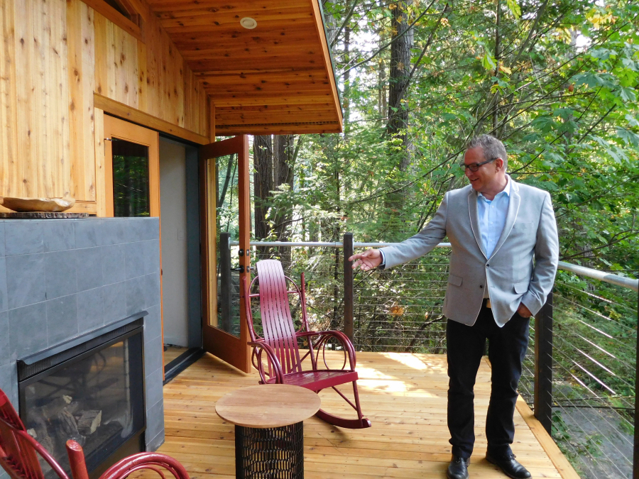 Todd Gillespie, sales and marketing director, points out fun features of the treehouse, including this indoor/outdoor fireplace, complete with a wood carved tic-tac-toe board, two rocking chairs and a table.