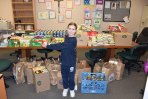 Third-grader Katie Jackson stands with some of the items she helped collect for Pacific Crest Academy's  annual food drive. Katie and her dad, Harlan, helped double the food collected by inquiring at Chuck's Produce about donations to the efforts. (Contributed photo)