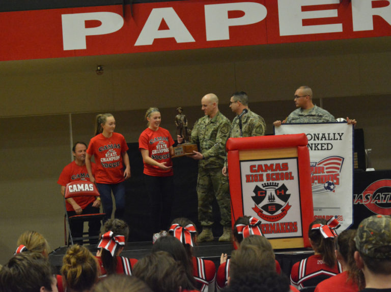 Members of the Army National Guard present Camas soccer captains Hannah Taie and Sabine Postma, and head coach Roland Minder, a trophy for earning the No.