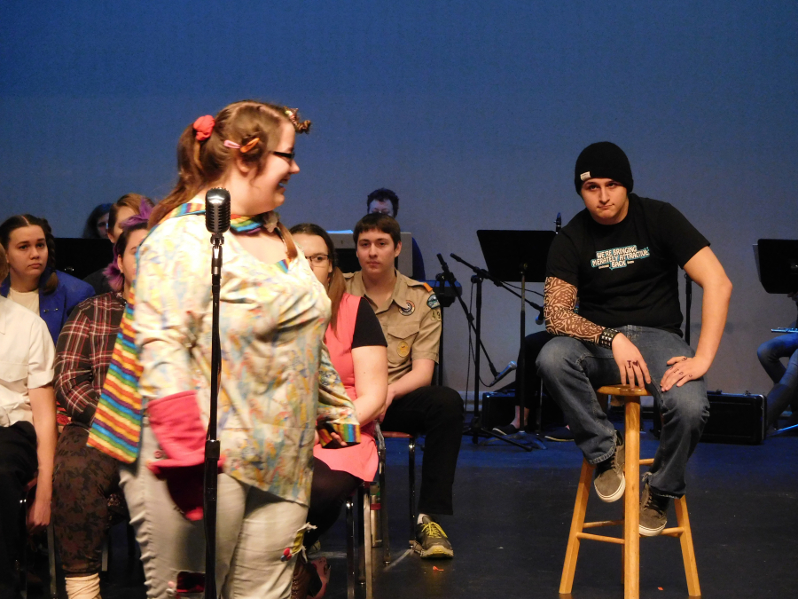 Leaf Coneybear (Shelly Morgan) checks a spelling word with the judges as Mitch Mahoney (Gabe Heinrich) looks on. 