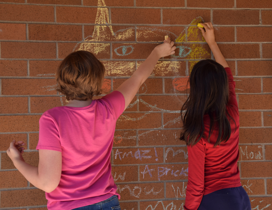 Students Ashlynn Smith, left, and Lana White, right, draw with chalk on the original Jemtegaard building. The two will start eighth grade in the new Jemtegaard building. (Photo by Tori Benavente/Post-Record)