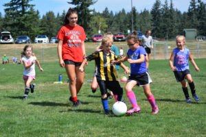 Camas High School senior Fallisitie DePasquale encourages children to keep moving the soccer ball during a youth camp, for 5- to 8-year-olds, Tuesday, in the fields on Ione Street, beside Doc Harris Stadium. 