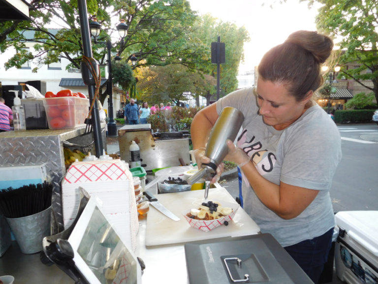 Arika White, owner of Hello Waffle, adds whipped cream to a  blueberry and banana waffle during Girls Night Out, Sept. 28, in downtown Camas. She provided free samples of waffles topped by Nutella hazelnut spread at the annual event that raises money for the Pink Lemonade Project and the Ovarian Cancer Alliance of Oregon/Southwest Washington. White, a vendor at the Camas and Vancouver farmers markets for three years, has opened a food cart in Camas.