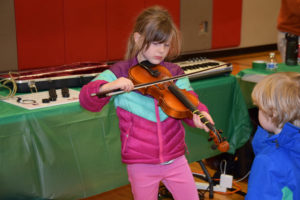 Emily Lampmann, a first-grader at Hathaway Elementary School, plays a violin provided by Opus School of Music, during her school's Dec. 6 Dream Big event, while her younger brother, Alexander Lampmann, watches. 