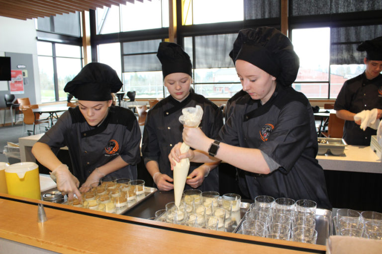 Junior Sarah Oster (left), and sophomores Mattie Wakefield (center) and Alexis Garrett (right), fill cups with sponge cake cutouts and tiramisu cream filling.