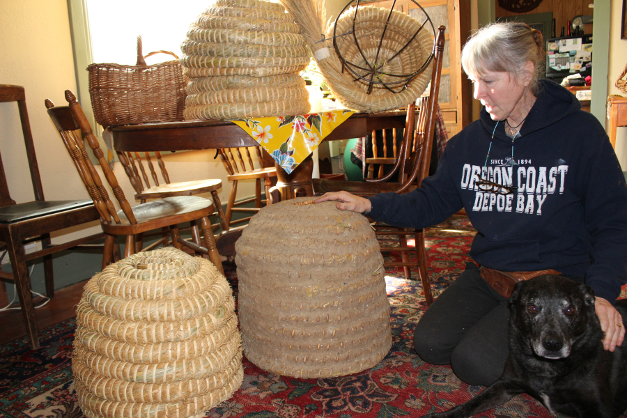 Susan McElroy-Knilans and her dog, Mazel Tov, sit next to her skep beehivees on Thursday, Feb. 8. Knilans makes her skeps with straw she cuts from Camas parks, with the permission of the city.