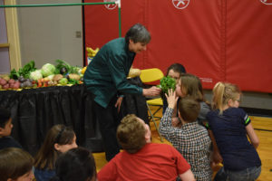 Sharon Whalen, from Duck Delivery Produce, holds cilantro for Hathaway Elementary School students to smell and identify the differences between similar leafy greens during the Well-Being Fair at Hathaway on April 20. The students learned about nutrition, recycling, fruits and vegetables and gardening during the fair. 