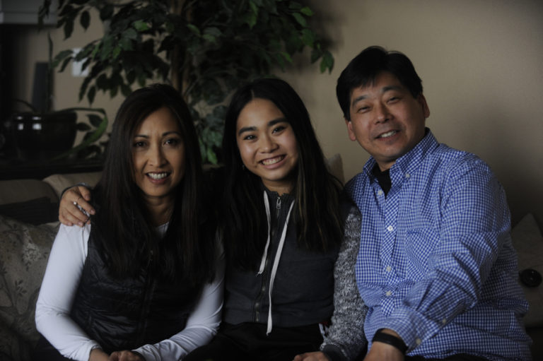 Kaylee Sugimoto (center) sits with her mom, Marnie (left), and dad, Glen (right).
