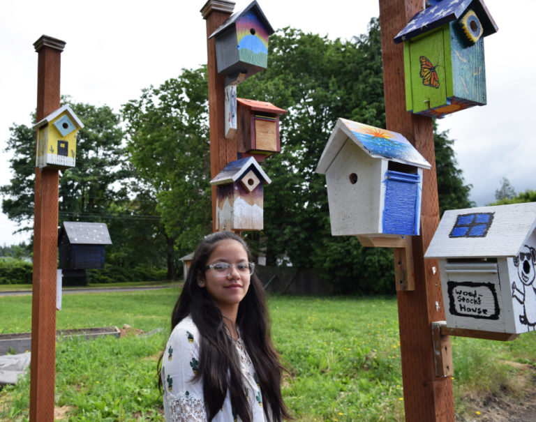 Jemtegaard Middle School eighth grader Annabella Arriola stands beneath the birdhouse she painted a rainbow on during Jemtegaard Club 8 after-school program, Saturday, June 23. An artists&#039; reception was held for the 10 Jemtegaard Middle School students who decorated the houses that line the Washougal City Hall parking lot.