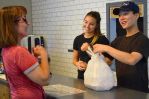 Longtime Hana Foods patron Sheryl Obegi  (left) accepts her to-go order from Hana servers Sophie Eagle (center) and Eric Park (right) on the restaurant's re-opening day, Monday, June 25.