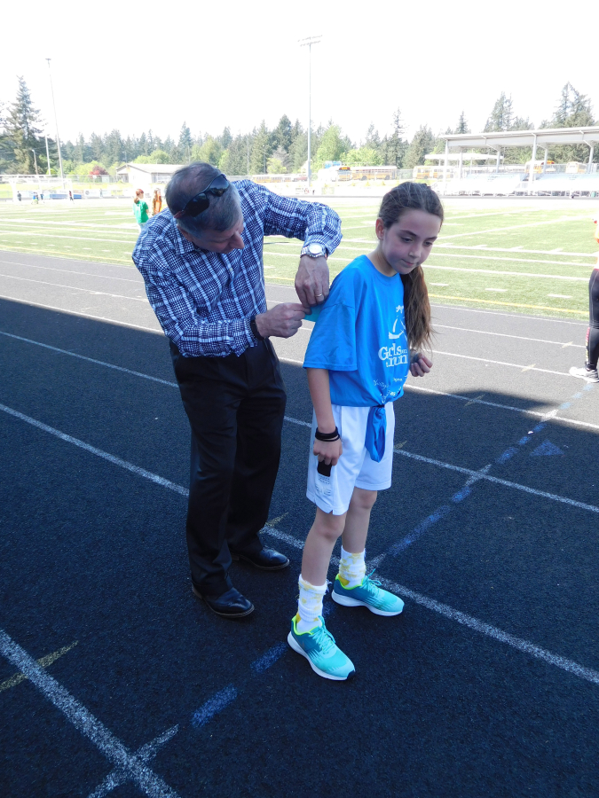 John DiPalma attaches a pin to a student&#039;s race bib to signal the completion of another lap during a training run for a 5K at Camas&#039; Doc Harris Stadium.