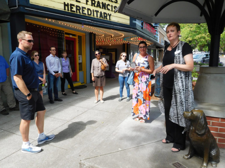 Carrie Schulstad (right), executive director of the Downtown Camas Association (DCA), talks about Camas businesses, while standing next to &quot;Millie,&quot; the bronze artwork, in front of the Liberty Theatre, in the historic downtown Camas district, July 13, during the Columbia River Economic Development Council&#039;s Main Street Day tour.