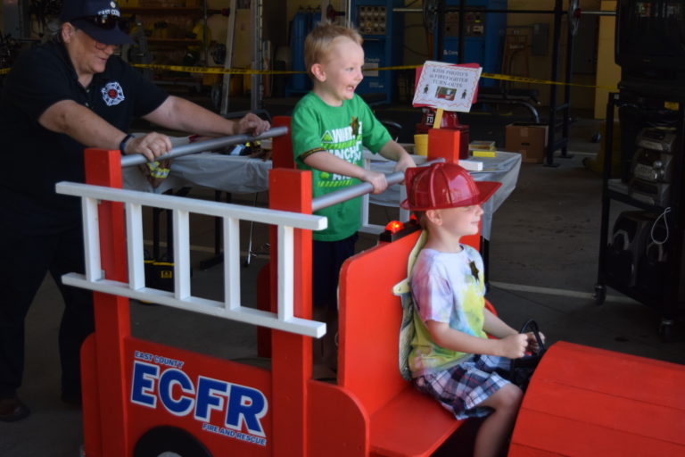 Brayden Weaver, 6, steers the wheel of the East County Fire and Rescue (ECFR) mini-engine while brother Reynold Weaver,4,  enjoys the ride from the top, Sunday, July 29. The ECFR held its annual open house for the community. 
