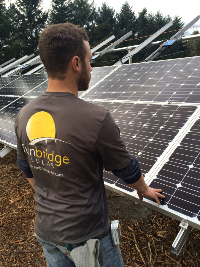 Garret Little, assistant project manager of Sunbridge Solar, checks to make sure an array of solar panels is straight and level. Sunbridge Solar, an eight-year-old company, will relocate from Vancouver to Washougal in September.