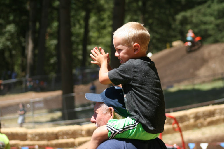 A young fan cheers on his favorite motocross racers with the help of his grandfather on Saturday, July 28.