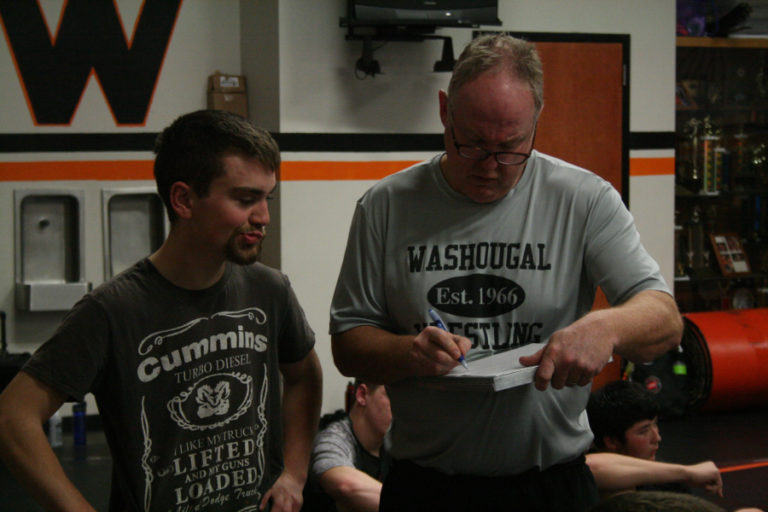 Head Washougal boys wrestling coach John Carver (right) signs paperwork for one of his wrestlers at practice.