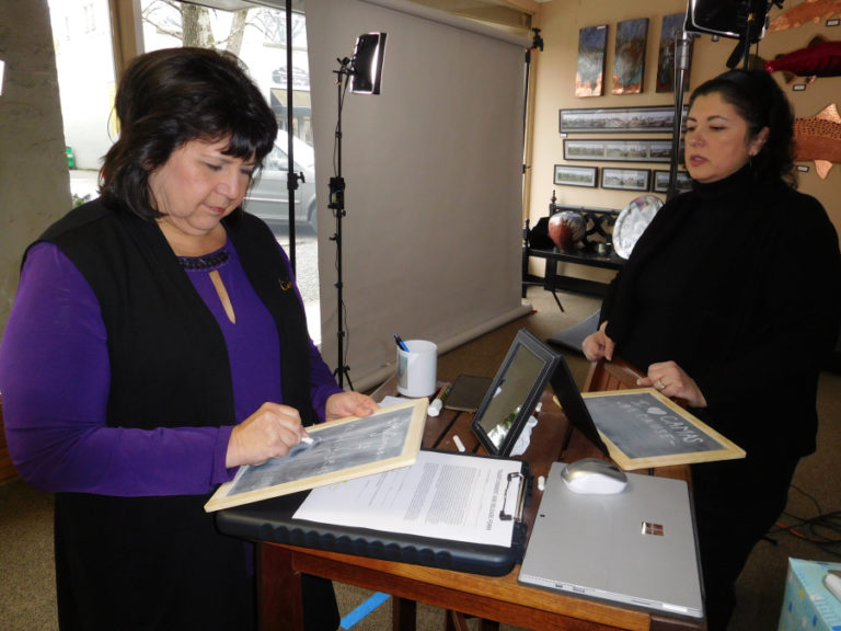 Terri Sauer, co-owner of the Camas Hotel, writes that she loves Camas because it is "a hidden gem," while Flowerpot Media Chief Executive Officer Laura Bakken looks on, Friday, Feb. 8, in Camas Gallery.