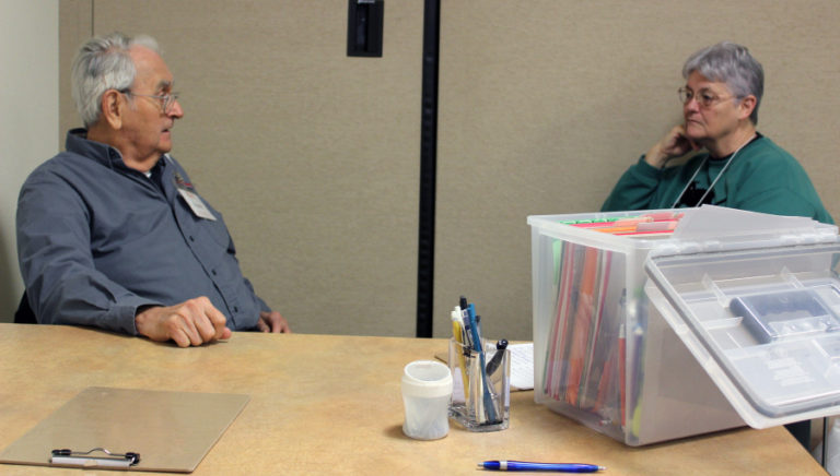 Tax-Aide volunteers Virgil Myers (left) and Vicki Smith (right) sit at the entrance of the AARP Foundation Tax-Aide site at the Camas Public Library, on Feb. 14.