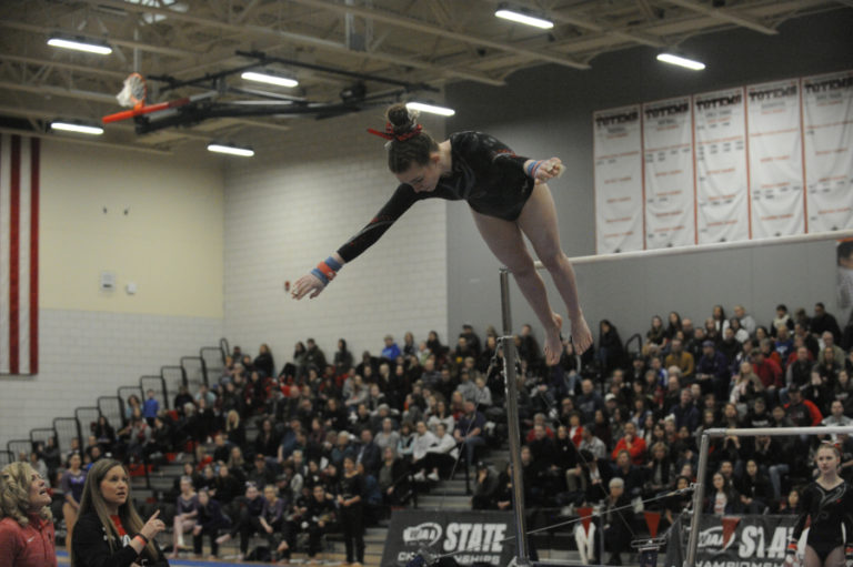 All-around state champion Shea McGee soars during a dismount from the bars with her coaches at her side.