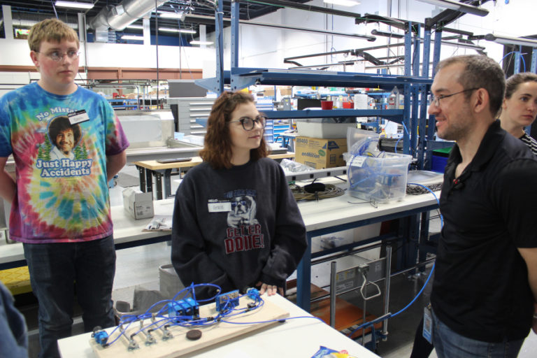 From left to right, Gavin Ragan, 17, and Grace Callaway, 16, listen to SIGMADESIGN systems engineer Anthony Gittins describe equipment that can make exact cuts -- in this case, for an April 25 &quot;Take Your Child to Work&quot; event, to cut an Oreo cookie into two equal halves.