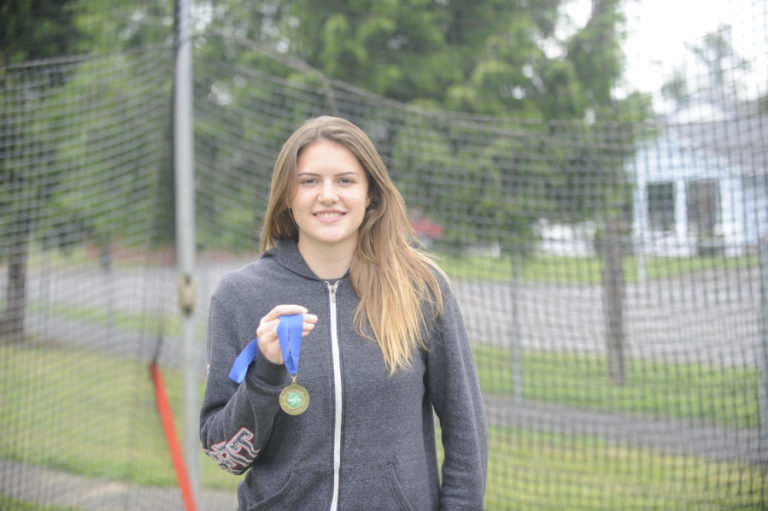 State champion discus thrower Kiersten De La Rocha holds her gold medal inside the throwing area at Washougal High School where she learned her craft.