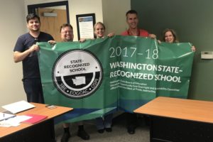 From left to right, Jemtegaard Middle School (JMS) staff members Jason Foster, Scott Rainey, Michelle Massar and David Cooke, and former JMS associate principal Tami Culp (right) hold a banner proclaiming the school's state recognition for the 2017-18 school year at the Washougal School District's board of directors meeting June 11. (Doug Flanagan/Post-Record)