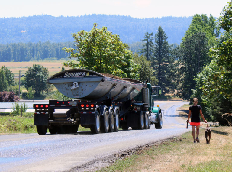 Rachel Grice, of Washougal, walks her dog near her home in July 2018 while a truck from a nearby Washougal rock mine passes by. Grice is one of more than a dozen Washougal residents who are, along with the nonprofit Friends of the Columbia Gorge group, hoping to halt mining operations at the Washougal Rock Pit. The Gorge Commission is expected to issue an oral ruling on Aug. 13.