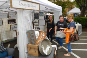 Vendors from the Washougal-based honey BE designs listen to a shopper at the Downtown Camas Vintage and Art Faire in August 2018. The annual event, which features indoor and outdoor furniture, home and garden items, artwork and handmade jewelry, will return to the streets of downtown Camas in August 2021. (Post-Record file photo)