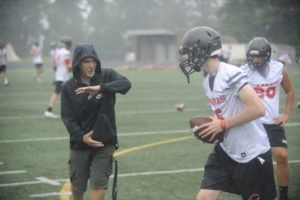 Camas High School football head coach Jon Eagle (left) gives some pointers to quarterback Jake Blair (center) about handing off footballs in heavy rain. (Photos by Wayne Havrelly/Post-Record)