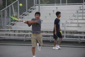 Micheal Lee hits a backhand during a competition drill called "king of the hill" with Sunny Wang in the background. (Photos by Wayne Havrelly/Post-Record)