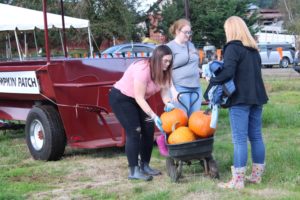 Carly Sorensen (left), of Troutdale, Ore., drops a pumpkin into a wagon Saturday, Oct. 5, at Waltons Farms in Camas while her sister, Katie (center), and mother, Christine (right), look on. (Doug Flanagan/Post-Record)