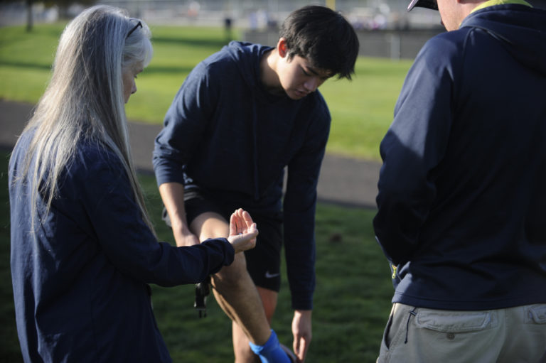 The Camas High School cross country coaching staff analyzes Luc Utheza&#039;s strained calf during a recent practice session.